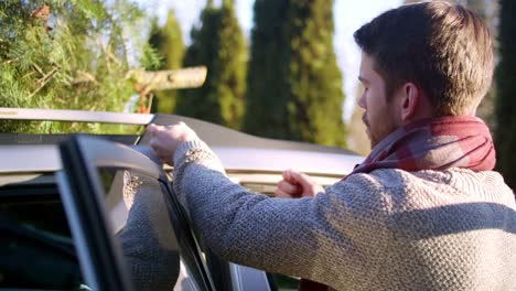 Joven-atado-a-un-árbol-de-Navidad-para-el-coche-con-la-cuerda