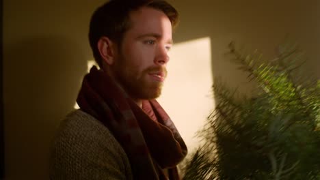 Young-man-holding-up-a-Christmas-tree-at-home