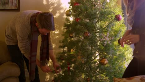 Joven-marido-y-mujer-poniendo-adornos-en-un-árbol-de-Navidad