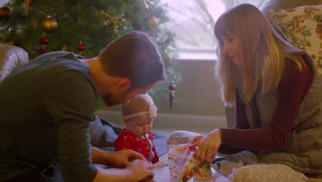 Eltern-öffnen-geschenke-mit-ihrem-Baby-vor-dem-Baum-am-Weihnachtsmorgen