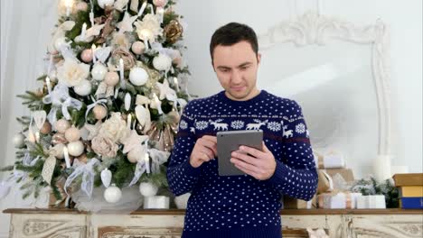 Young-man-in-Christmas-knitwear-checking-up-his-tablet