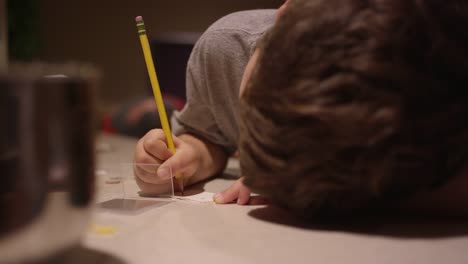 A-boy-sitting-at-the-kitchen-counter,-writing-and-putting-a-christmas-sticker-on-a-piece-of-paper