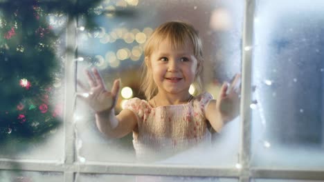 On-Christmas-Eve-Cute-Little-Girl-Looks-Through-the-Window-and-Smiles.