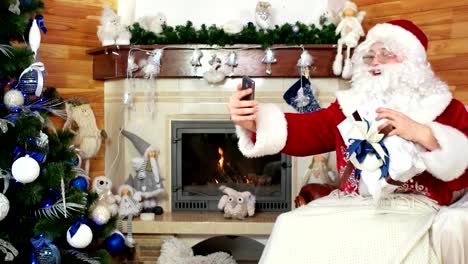 santa-taking-photo-with-present,-papa-noel-posing-for-selfie,-room-with-fireplace,-santa-claus