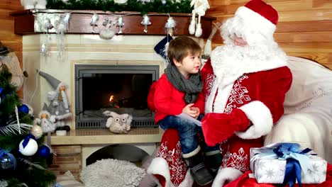 Junge-sitzt-auf-Santas-Schoß-Kind-geben-Nikolaus-seine-Cristmas-Wunschliste-in-Umschlag,-Urlaub