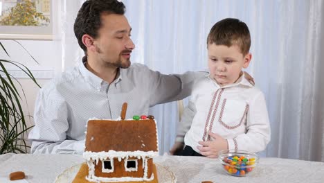 Kleinen-Sohn-mit-Vater-schmückt-ein-Lebkuchenhaus-mit-einem-bunten-Bonbons