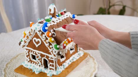 The-woman-writes-a-text-with-cream-on-the-roof-of-gingerbread-house