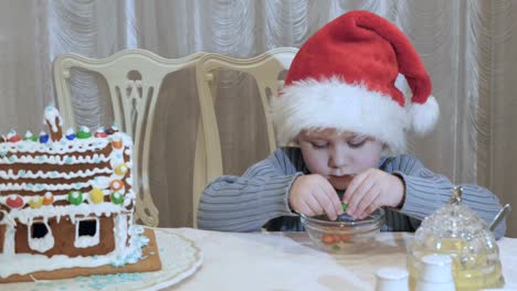 Cute-little-boy-in-santa's-hat-palys-with-colorful-candies-at-the-table