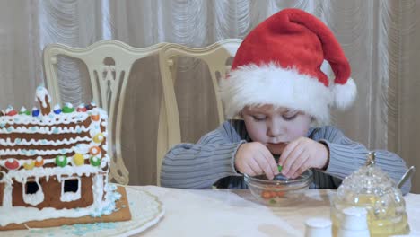 Niño-lindo-en-palys-de-sombrero-de-santa-con-coloridos-caramelos-en-la-mesa