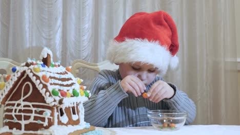 Niño-lindo-en-sombrero-de-santa-pela-un-caramelo-de-chocolate-en-la-cocina