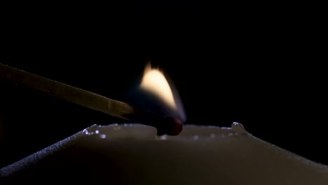 Slow-motion-macro-footage-of-a-white-candle-lit-by-a-match-on-a-dark-background