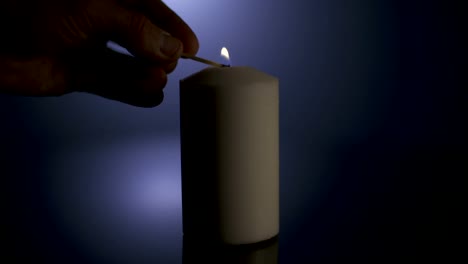 Slow-motion-macro-footage-of-a-white-candle-lit-by-a-match-on-a-dark-background