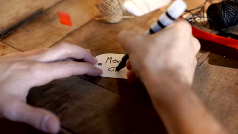 Young-adult-man-writing-christmas-card-on-white-label-on-old-wooden-table-in-cozy-home-indoor