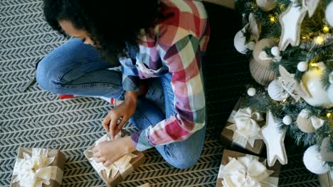 Top-view-of-Attractive-mixed-race-girl-packing-gift-box-near-Christmas-tree-at-home