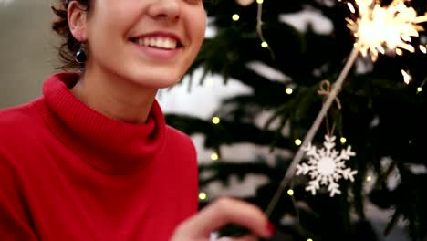 Glücklich-attraktive-junge-Frau-sitzt-auf-dem-Boden-durch-den-Weihnachtsbaum-feiert-Weihnachten-mit-Wunderkerzen-und-Blick-in-die-Kamera