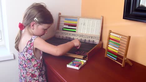 Sweet-little-girl-plays-with-abacus-and-writes-on-blackboard-with-chalk.-Preschool-concept,-childhood-concept.-Toy-abacus-with-Czech-alphabet.-Cinematic-flare