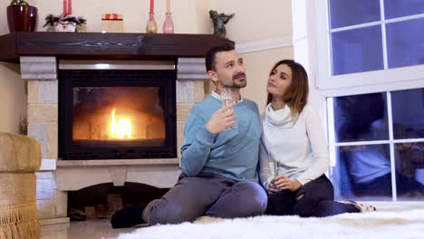 Pareja-feliz-bebe-champán-relajante-junto-a-la-chimenea