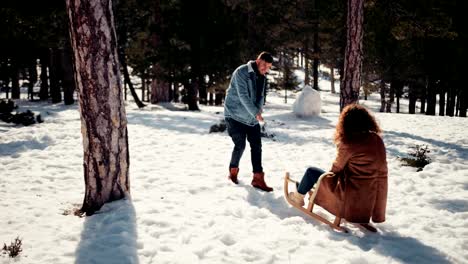 Boyfriend-pulling-girlfriend-on-sled-in-snowy-forest-park
