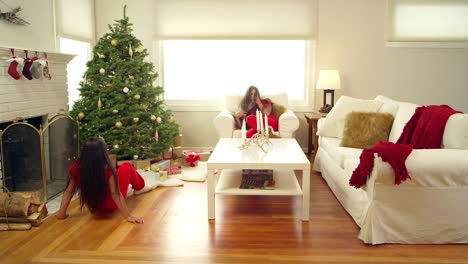 Two-girls,-sisters,-run-into-the-living-room-on-Christmas-morning-and-start-to-shake-their-presents