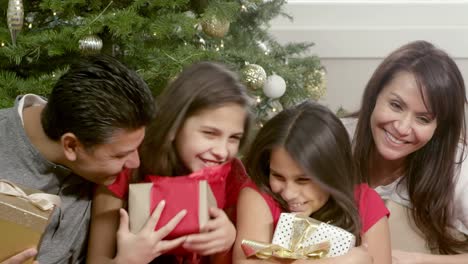 A-family-sitting-under-their-christmas-tree-holds-their-presents-and-pose-for-a-picture