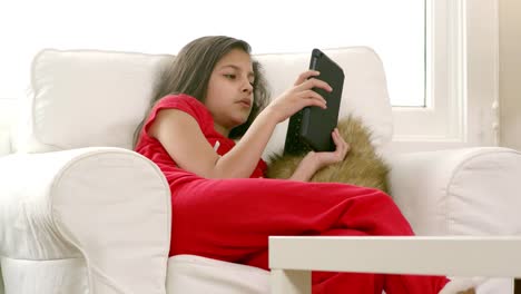 A-girl-sits-on-a-chair-in-the-living-in-her-pajamas-and-stares-at-her-tablet