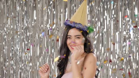 Beautiful-asian-woman-holding-glass-of-champagne-dancing-among-confetti-over-silver-glitter-background,-slow-motion