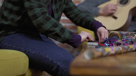 Young-woman-packing-Christmas-gift,-man-playing-guitar-in-background