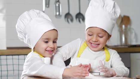 Two-little-girls-in-the-kitchen-prepare-food,-a-dessert-for-the-family.-As-they-learn-to-cook-they-start-playing-with-flour-and-smiling-each-other.