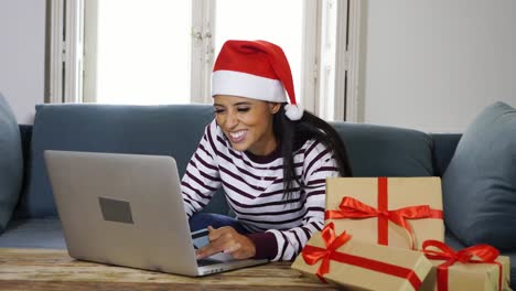 Frau-mit-roten-Pullover-und-Weihnachtsmann-Mütze-mit-Kreditkarte-auswählen-und-kaufen-Weihnachtsgeschenke-mit-Laptop-zu-Hause-begeistert-mit-Verkauf-über-das-Internet-und-Kreditkarte-Einrichtungen-in-Linie-einkaufen