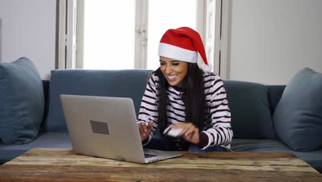 Woman-wearing-red-sweater-and-santa-claus-hat-holding-credit-card-choosing-and-buying-christmas-gifts-using-laptop-at-home-excited-with-internet-sales-and-credit-card-facilities-in-on-line-shopping