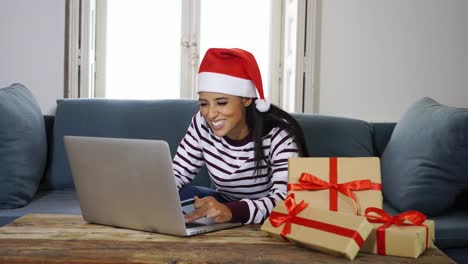 Frau-mit-roten-Pullover-und-Weihnachtsmann-Mütze-mit-Kreditkarte-auswählen-und-kaufen-Weihnachtsgeschenke-mit-Laptop-zu-Hause-begeistert-mit-Verkauf-über-das-Internet-und-Kreditkarte-Einrichtungen-in-Linie-einkaufen