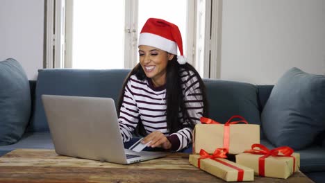 Frau-mit-roten-Pullover-und-Weihnachtsmann-Mütze-mit-Kreditkarte-auswählen-und-kaufen-Weihnachtsgeschenke-mit-Laptop-zu-Hause-begeistert-mit-Verkauf-über-das-Internet-und-Kreditkarte-Einrichtungen-in-Linie-einkaufen