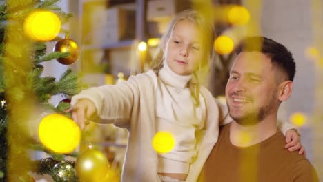 Padre-hija-sosteniendo-en-brazos-al-mismo-tiempo-decorar-árbol-de-Navidad