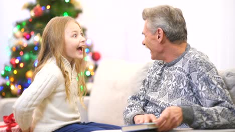 The-grandfather-read-a-book-and-take-a-gift-from-a-girl-near-the-christmas-tree