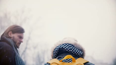 Back-view-happy-relaxed-young-man-and-woman-with-bright-yellow-backpack-walk-together-holding-hands-on-a-cold-snowy-day.