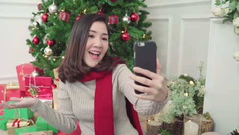 Alegre-feliz-joven-mujer-asiática-con-smartphone-selfie-de-Navidad-árbol-decorar-su-sala-de-estar-en-el-país-en-el-Festival-de-Navidad.-Mujer-de-estilo-de-vida-celebrar-Navidad-y-año-nuevo-concepto.