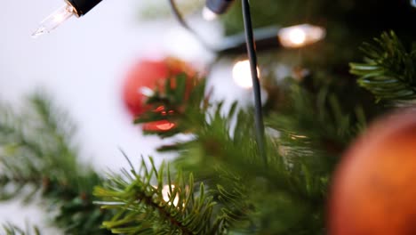 Handheld,-shallow-depth-of-field-close-up-of-glittering-baubles-hanging-on-a-Christmas-tree-with-fairy-lights