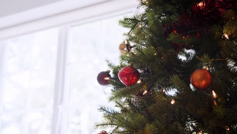 Downwards-tilt-shot-from-the-top-of-a-decorated-Christmas-tree-in-front-of-a-window