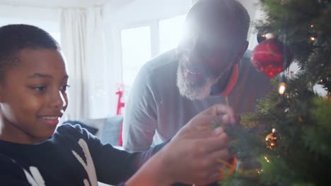 Abuelo-y-nieto-cuelga-adornos-de-árbol-de-Navidad-en-casa-junto