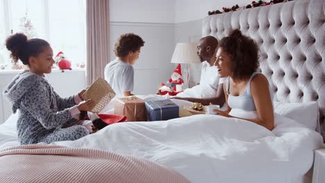 Excited-children-running-into-their-parents'-bedroom-and-jumping-onto-their-bed-with-Christmas-stockings-and-presents-on-Christmas-morning,-side-view