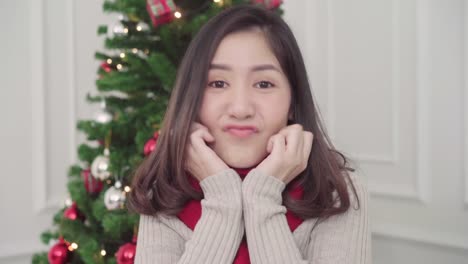 Cheerful-happy-young-Asian-woman-smiling-to-camera-in-her-living-room-at-home-in-Christmas-Festival.-Lifestyle-woman-celebrate-Christmas-and-New-year-concept.