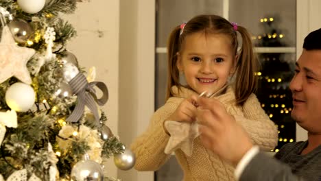 Feliz-padre-y-su-pequeña-hija-decorando-el-árbol-de-Navidad-en-casa