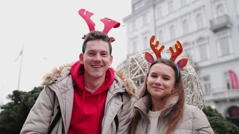 Lovely-Couple-standing-on-the-street-and-wear-Christmas-horns-on-head.-Smile-to-camera-and-give-a-hug