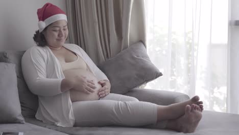 Asiatische-Frau-in-Santa-Suite-mit-ihrem-Baby-in-der-Schwangerschaft-Leben,-sitzen-auf-dem-Sofa-oder-Couch.