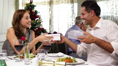 Pareja-feliz-teniendo-una-comida-juntos-y-de-intercambio-de-Navidad-regalos