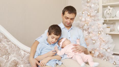 Junger-Vater-mit-Sohn-und-Neugeborenem-auf-dem-Sofa-in-Weihnachten