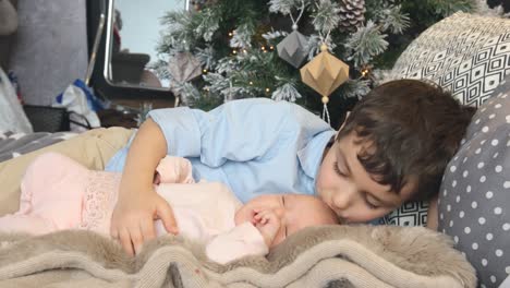 Little-brother-and-newborn-sister-lie-on-a-bed-in-Christmas