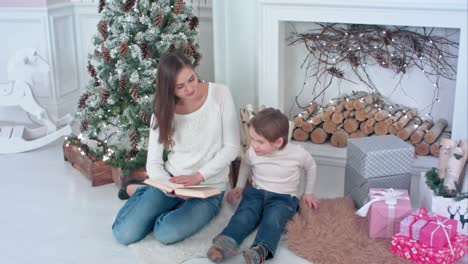 Young-mother-reading-book-to-distract-her-son-from-Christmas-presents