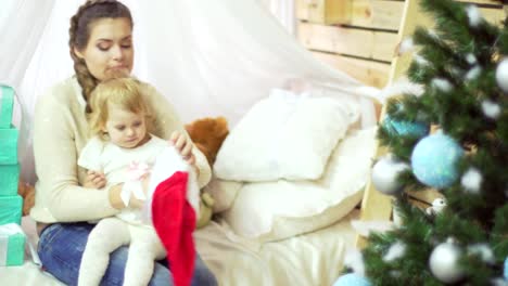 Madre-joven-feliz-jugando-con-su-bebé-dulce-en-un-decorado-cerca-del-árbol-de-Navidad