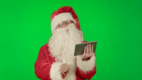 Cheerful-Santa-Claus-is-holding-a-tablet-in-his-hands-on-a-Green-Screen-Chrome-Key